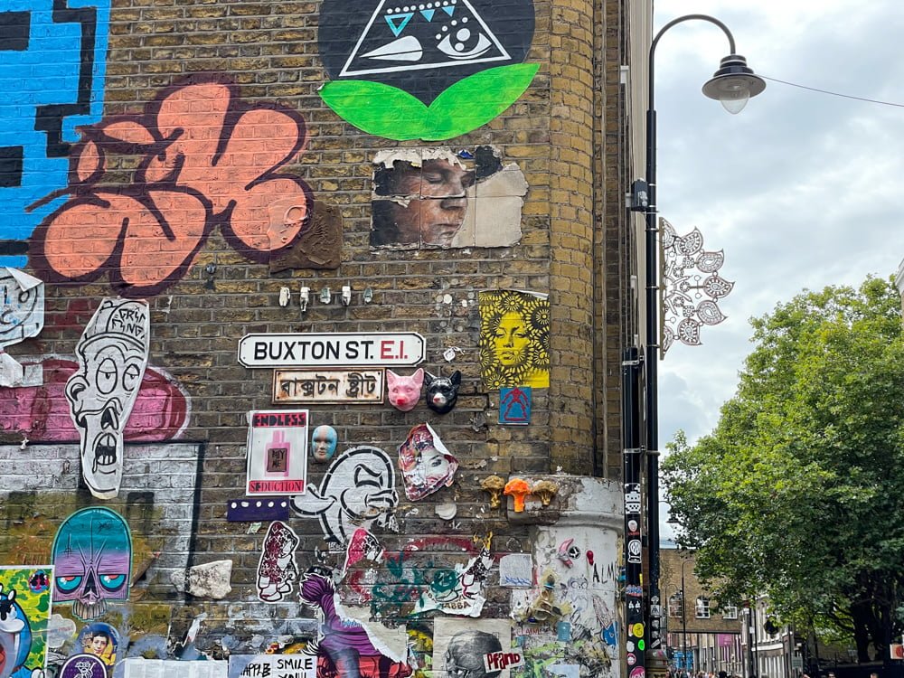 Street art surrounding the Buxton Street sign in Brick Lane, with English and Bengali lettering